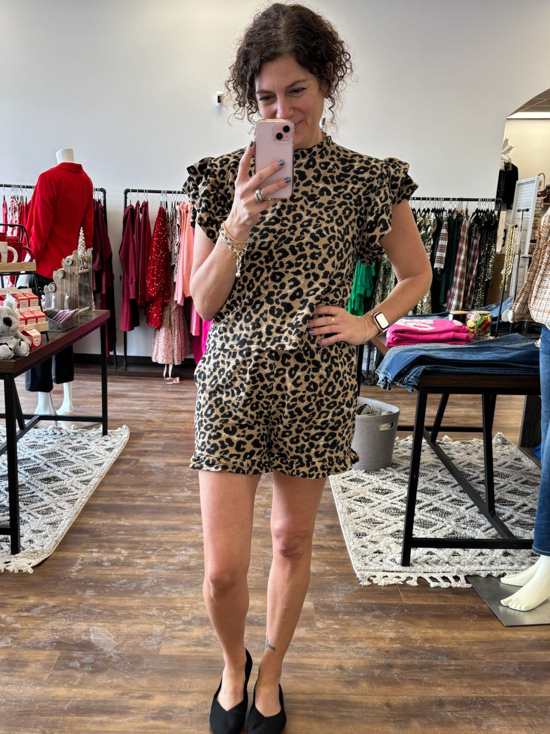 Woman taking a mirror selfie wearing a leopard print dress in a clothing store.