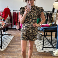 Woman taking a mirror selfie wearing a leopard print dress in a clothing store.