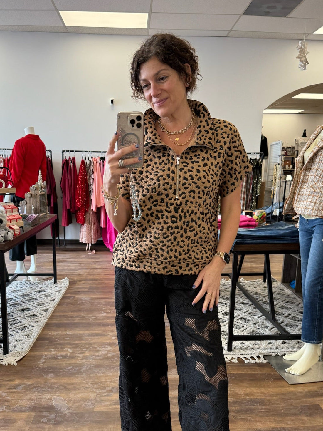 Woman taking a mirror selfie wearing a leopard print shirt and black pants in a store.