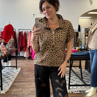 Woman taking a mirror selfie wearing a leopard print shirt and black pants in a store.